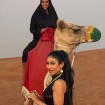 Two guests posing with a camel on the red dunes