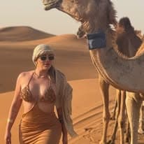 Guest walking beside camels through golden late-afternoon light on the dunes